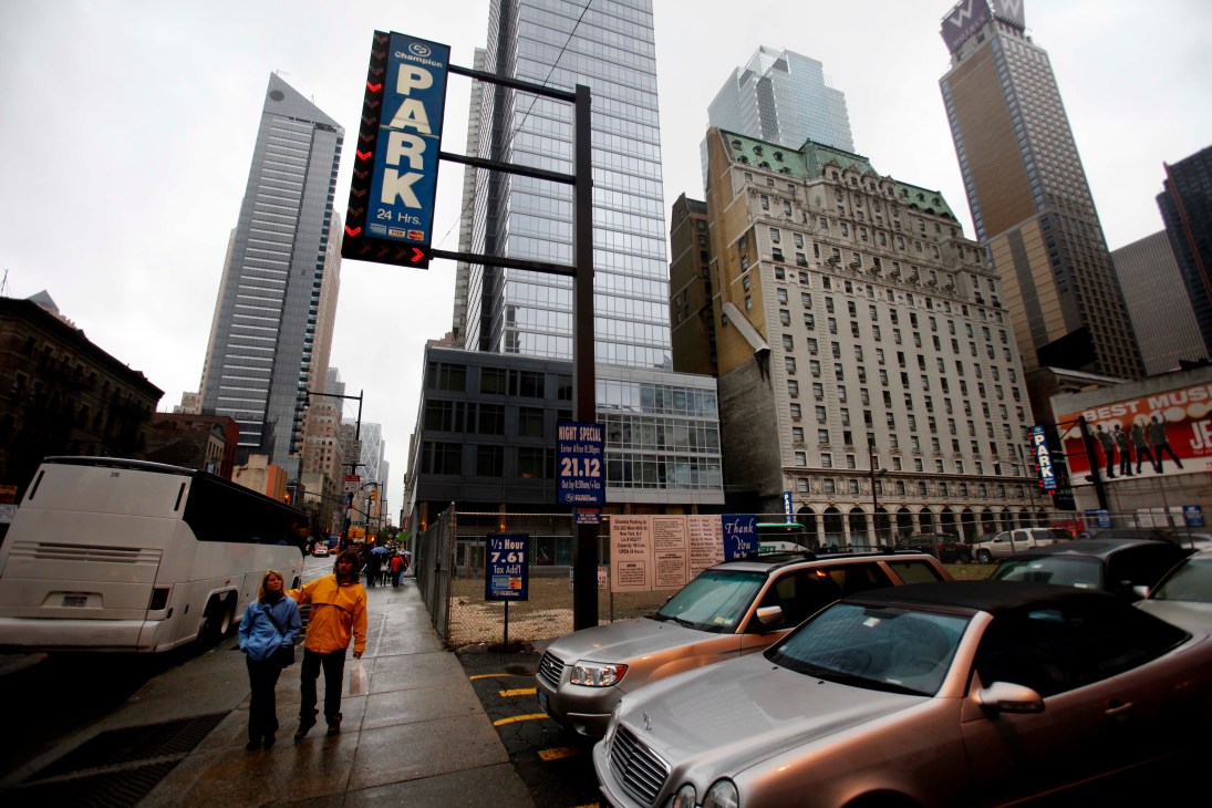 Urban street scene with parking sign, parked cars, pedestrians, and tall buildings in New York City.