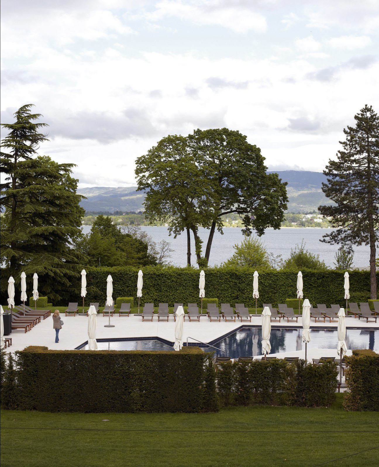 La Reserve hotel poolside with white umbrellas, lounge chairs, lake and Alpine mountains in background.