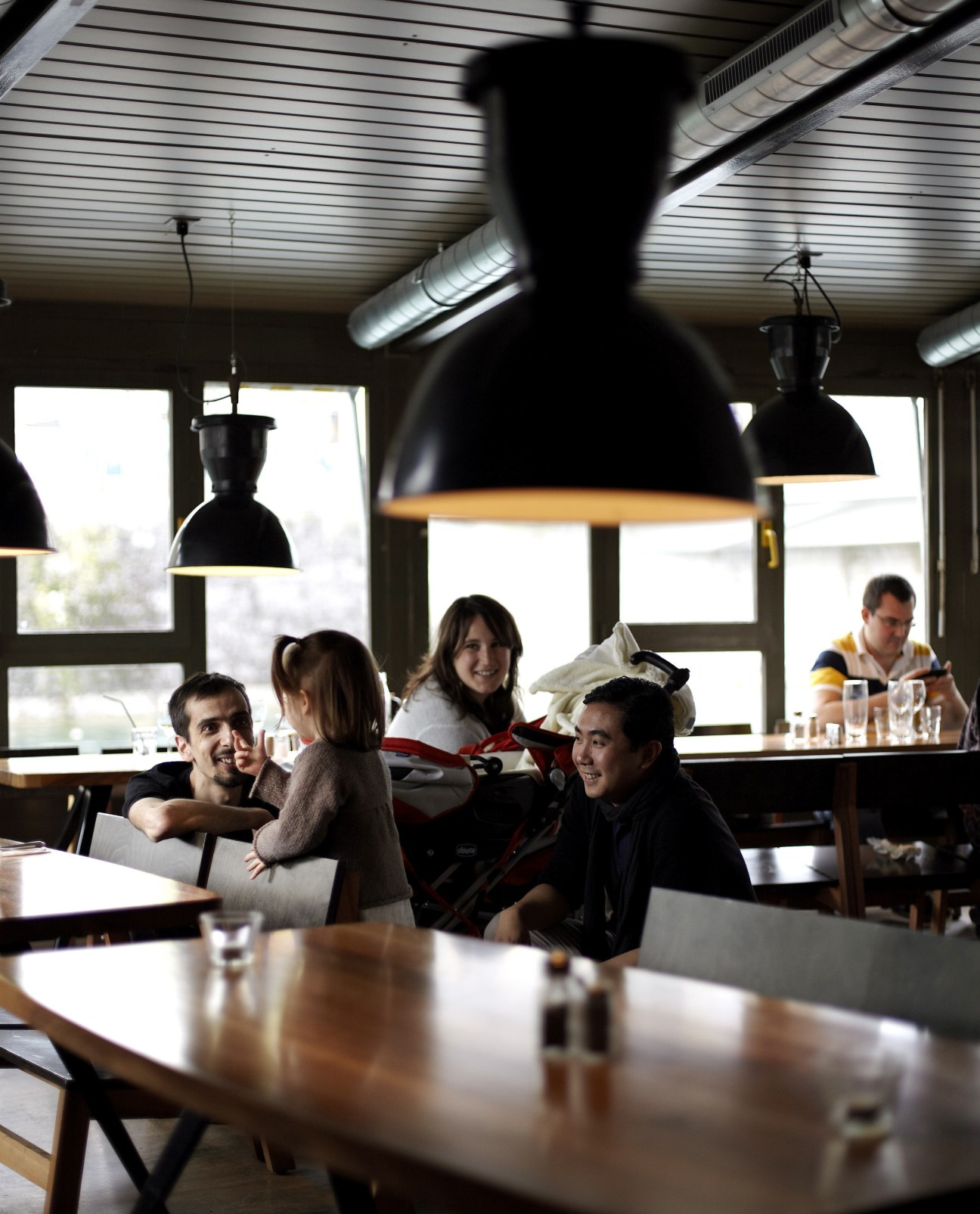 People dining at Brasserie des Halles de l'Ile with black pendant lamps overhead and large windows.