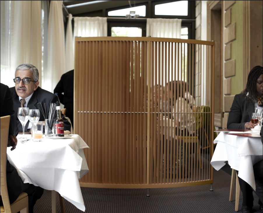 Diners seated at tables separated by wooden screen dividers in an upscale restaurant interior.