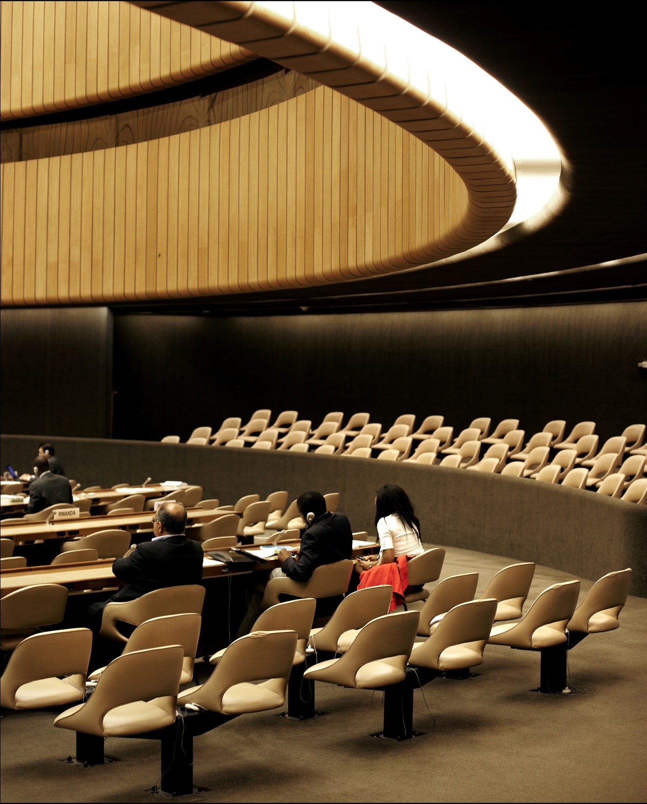 Interior of a United Nations meeting hall with curved ceiling and rows of cream-colored seats.