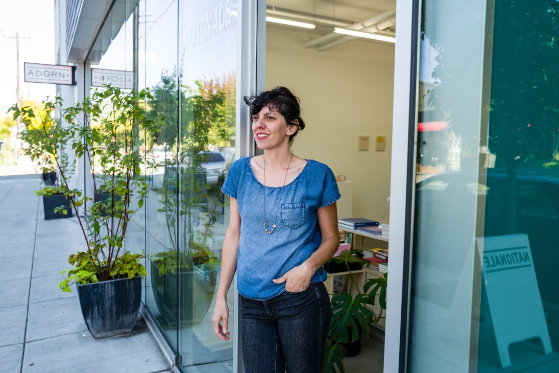Woman in blue denim shirt standing in doorway of Nationale shop in Portland with plants visible outside.