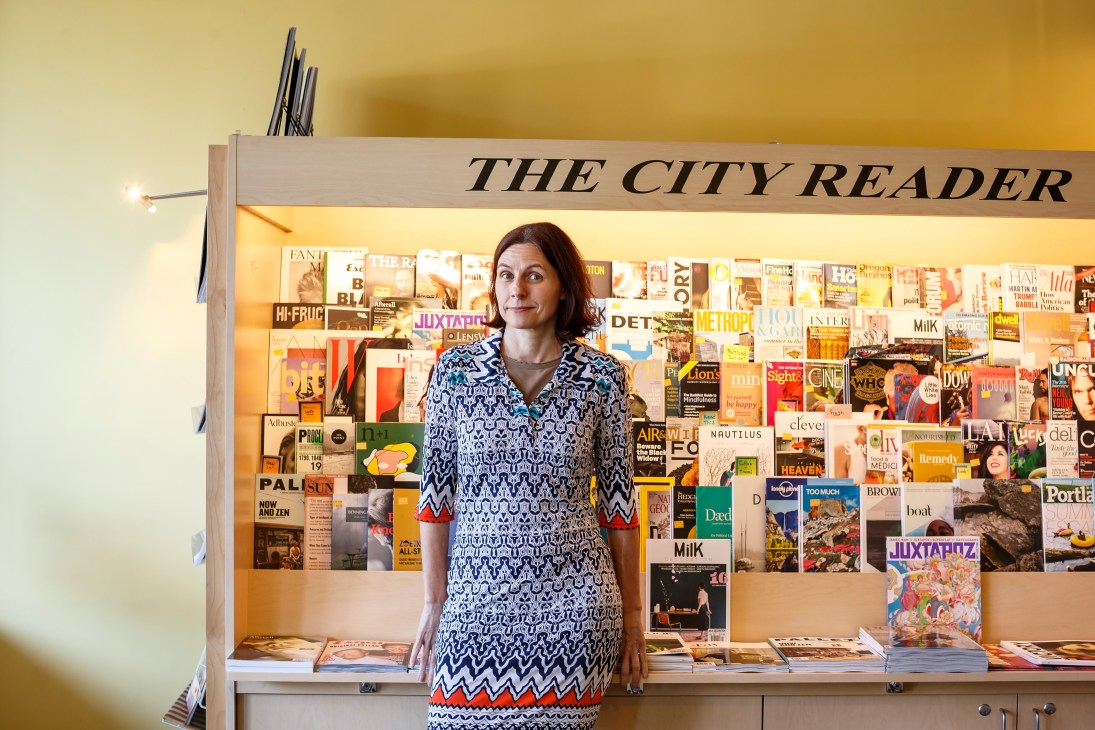 Karin Dibling stands in front of The City Reader newsstand displaying international magazines and publications in Portland.