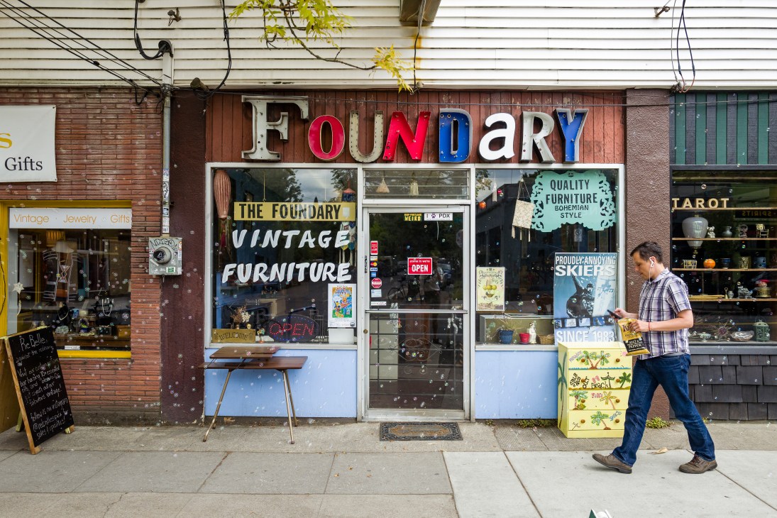 Man walking past The Foundary vintage furniture storefront with colorful signage on a Portland street.