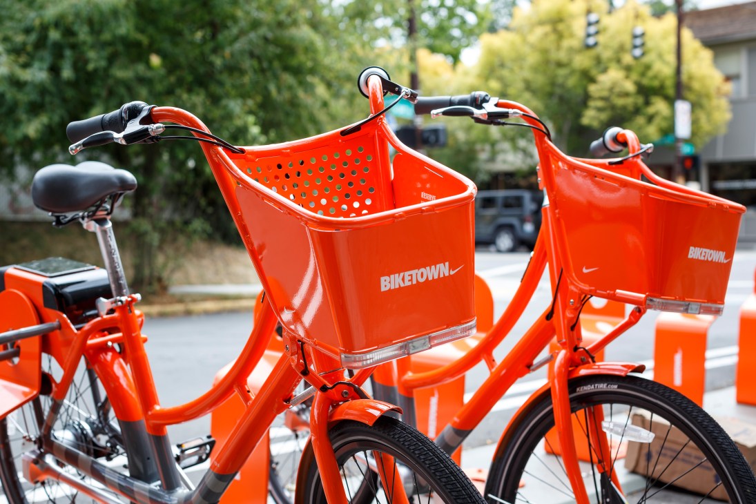 Bright red Biketown bike-share bicycles with perforated baskets parked at a station.