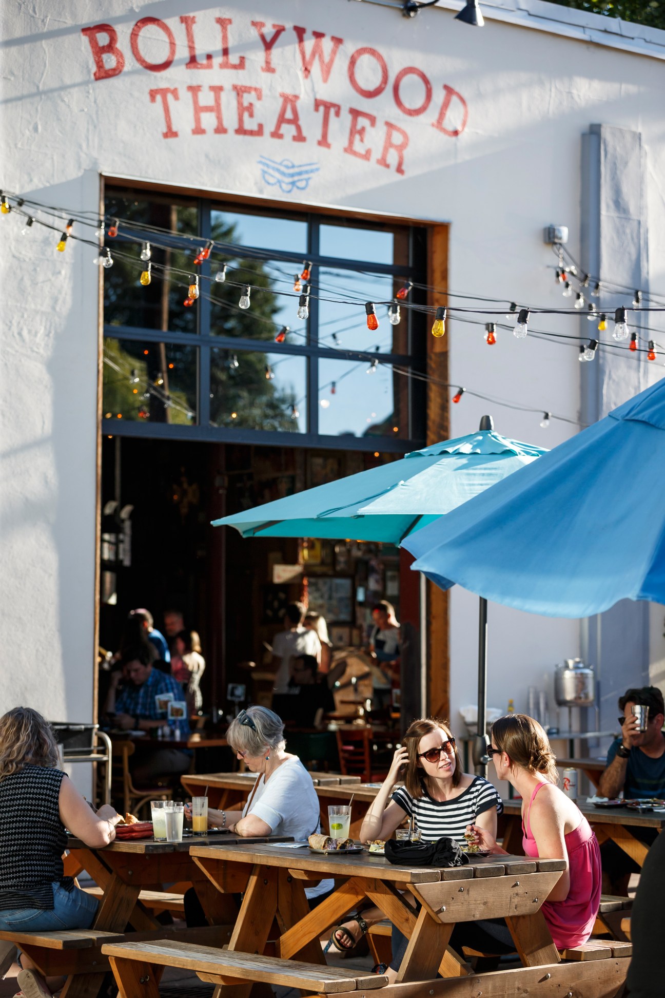 Exterior of Bollywood Theater restaurant with white wall signage and blue umbrellas shading outdoor seating area on Division Street, Portland.