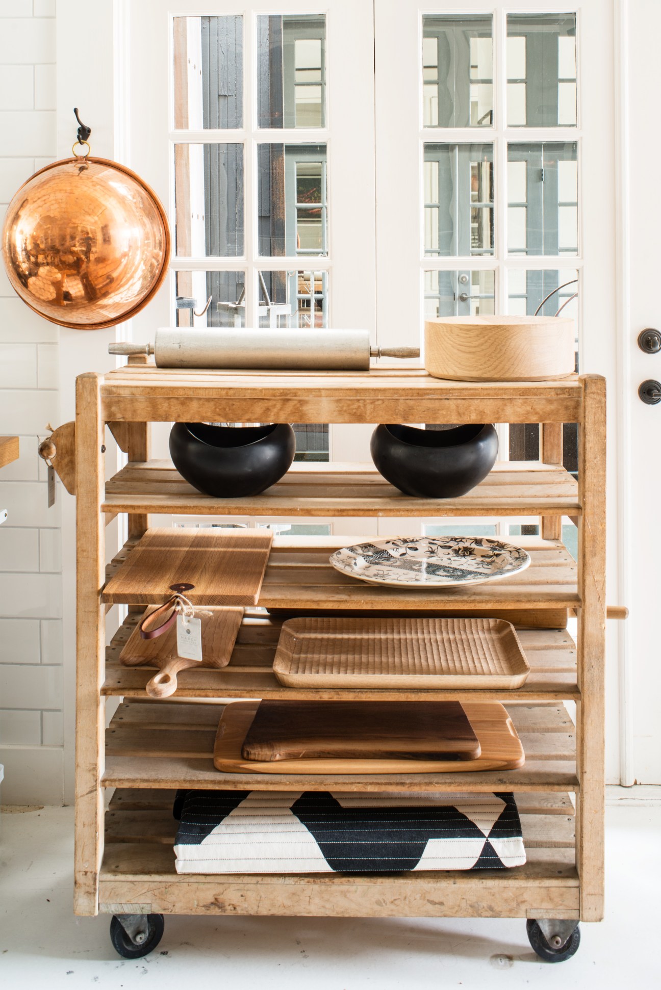 Wooden kitchen cart displaying copper cookware, wooden utensils, ceramic bowls and baking dishes.