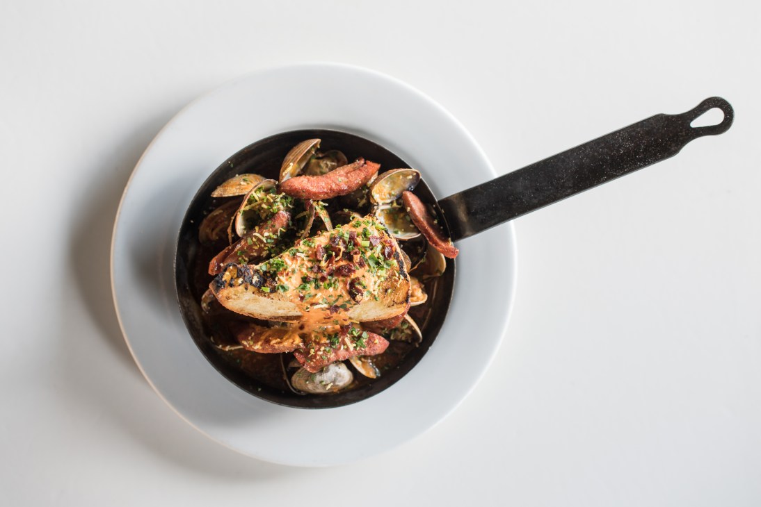 Clams and seafood in a black cataplana pan served on a white plate.