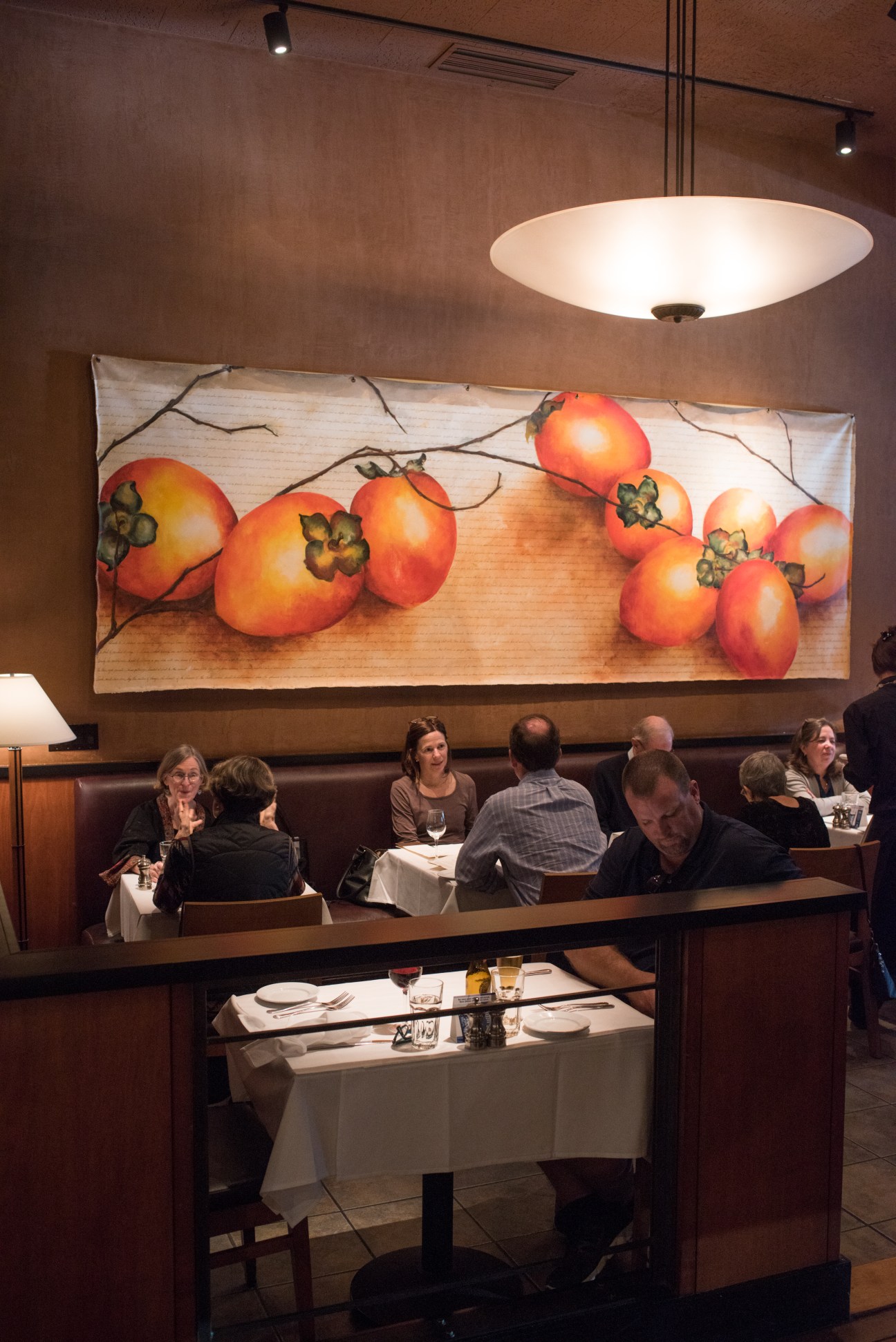 Restaurant interior with diners seated at a booth beneath a large tomato artwork.