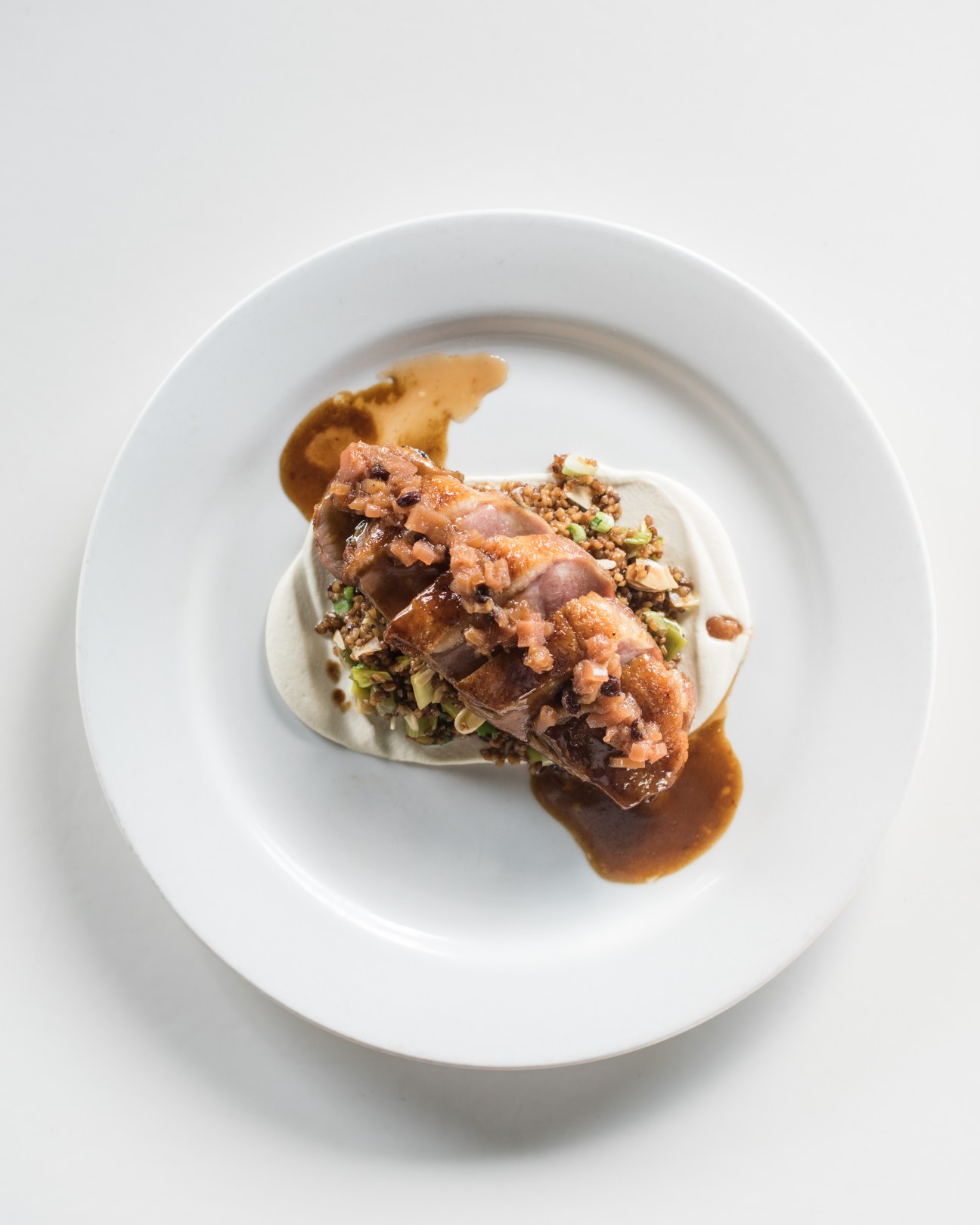 Duck breast served on almond skordalia with garnish and sauce on white plate.