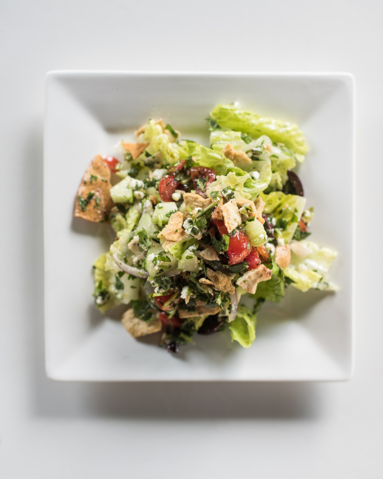 Fattoush salad with feta, mint and coriander served on a white square plate.