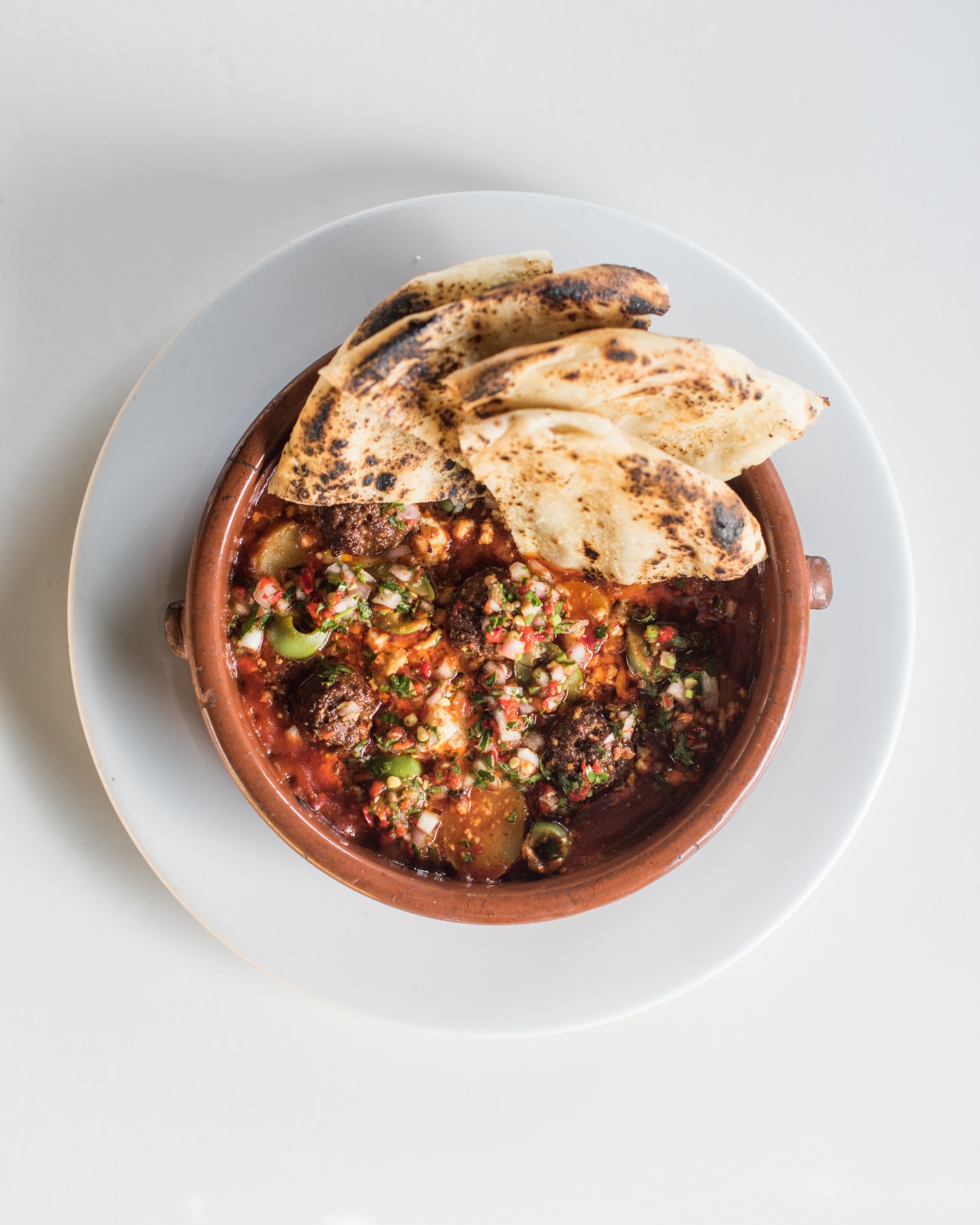 Lamb kefta topped with pickled chilli relish and homemade flatbread in a terracotta bowl.