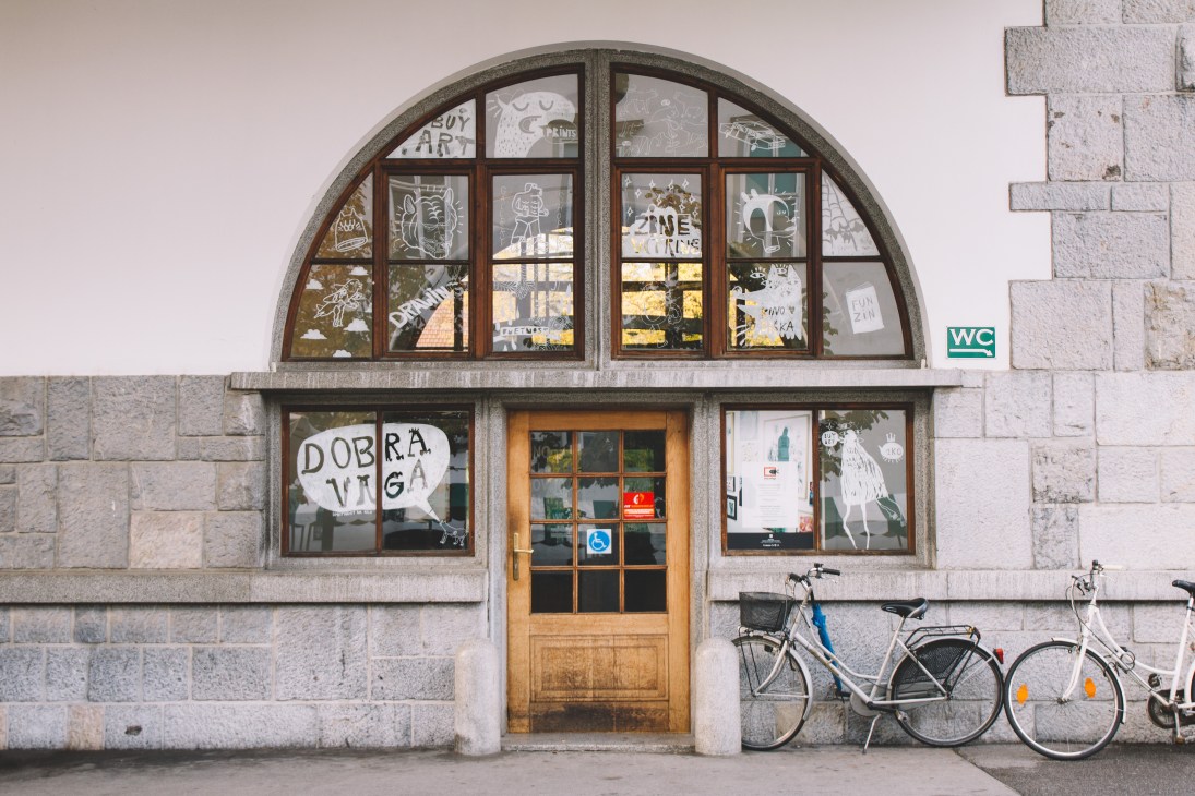 DobraVaga art gallery storefront with arched window, wooden door, and bicycles parked outside.