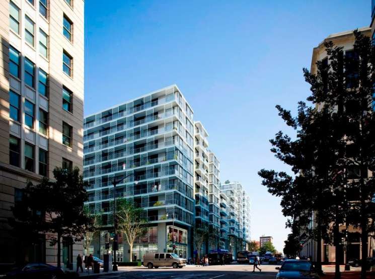 Modern residential building with glass balconies on a tree-lined urban street.