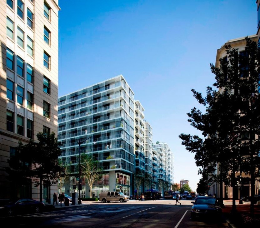 Modern residential building with glass balconies on a tree-lined urban street.