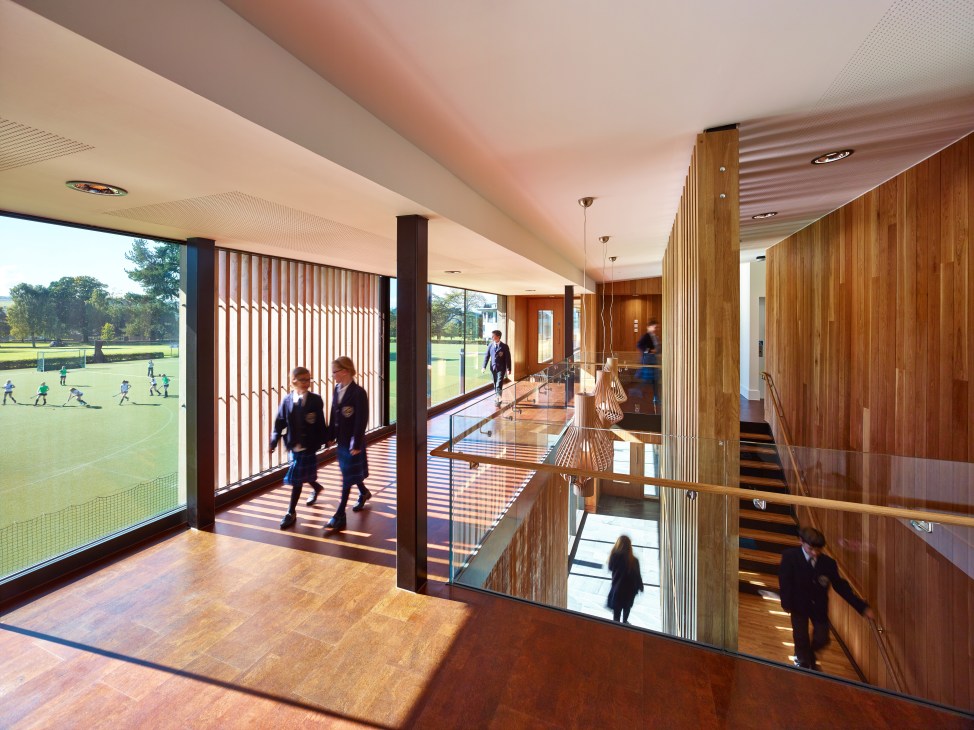 Modern interior with wooden finishes overlooking a sports field, featuring students and warm architectural details.