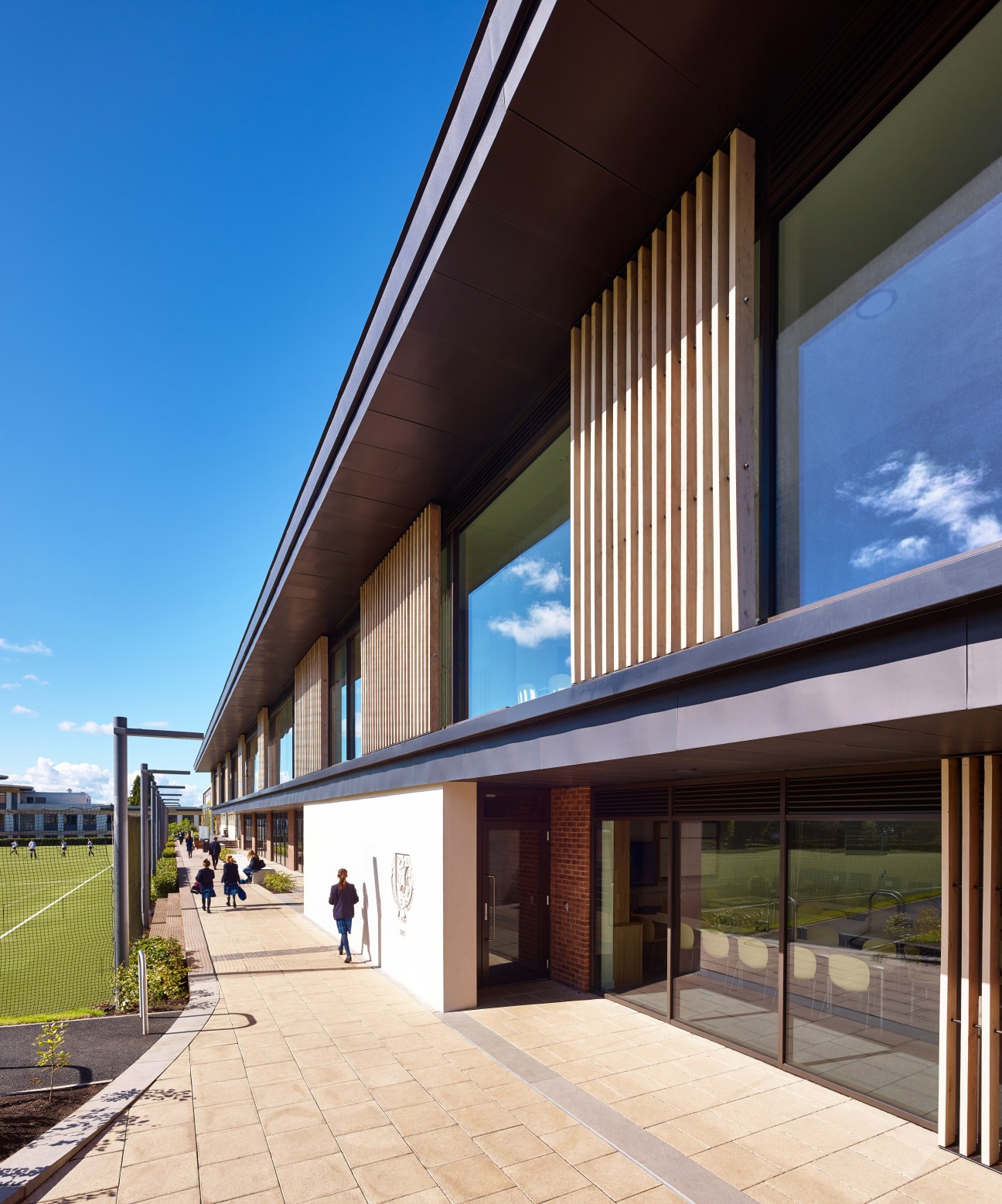 Modern Languages and Economics Building at Dollar Academy with brick and timber facade, large windows and wooden vertical slats overlooking a sports field.
