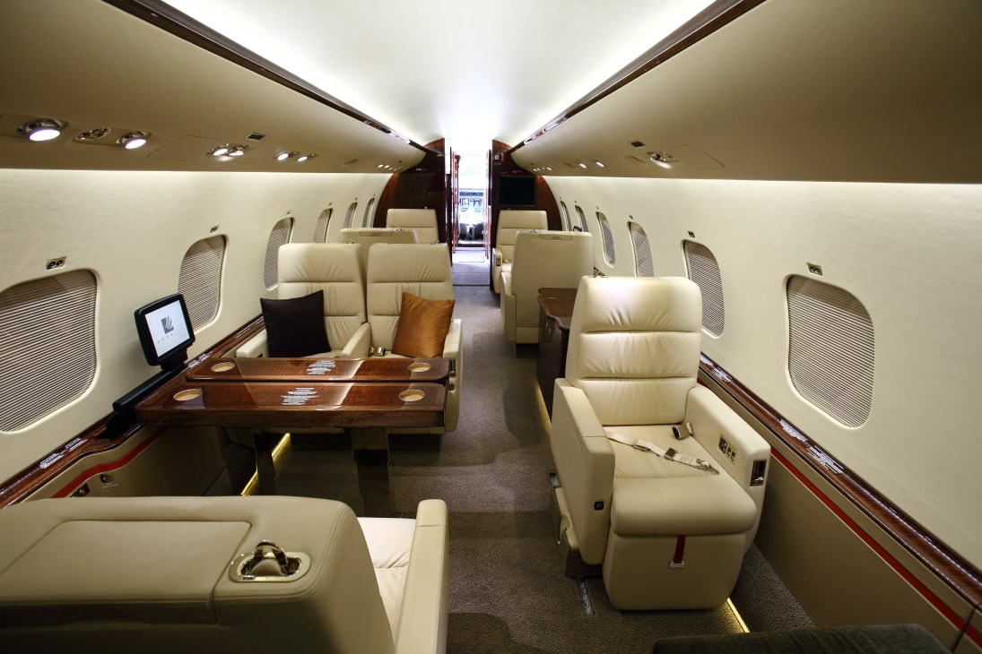 Interior of a Borajet aircraft cabin with cream leather seats, wooden tables, and modern lighting along the fuselage.