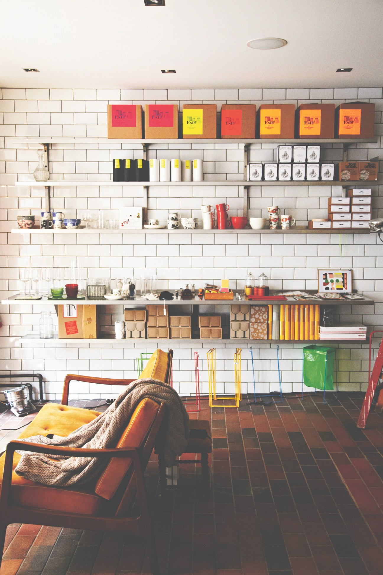 Interior of Dora design shop in Copenhagen featuring white subway tile walls, floating shelves with colorful products, and mid-century modern furniture.