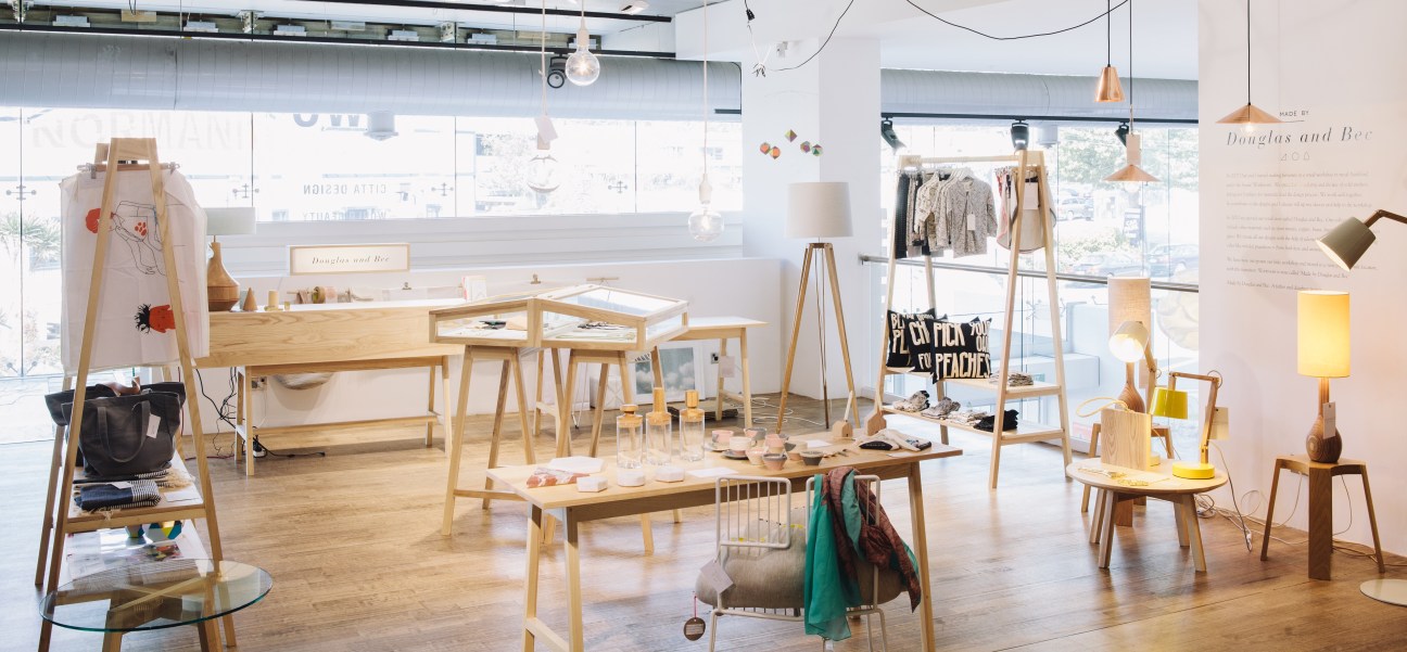 Interior of Douglas and Bec design store in Auckland showing wooden furniture, lighting displays, and merchandise on natural wood tables and shelving.