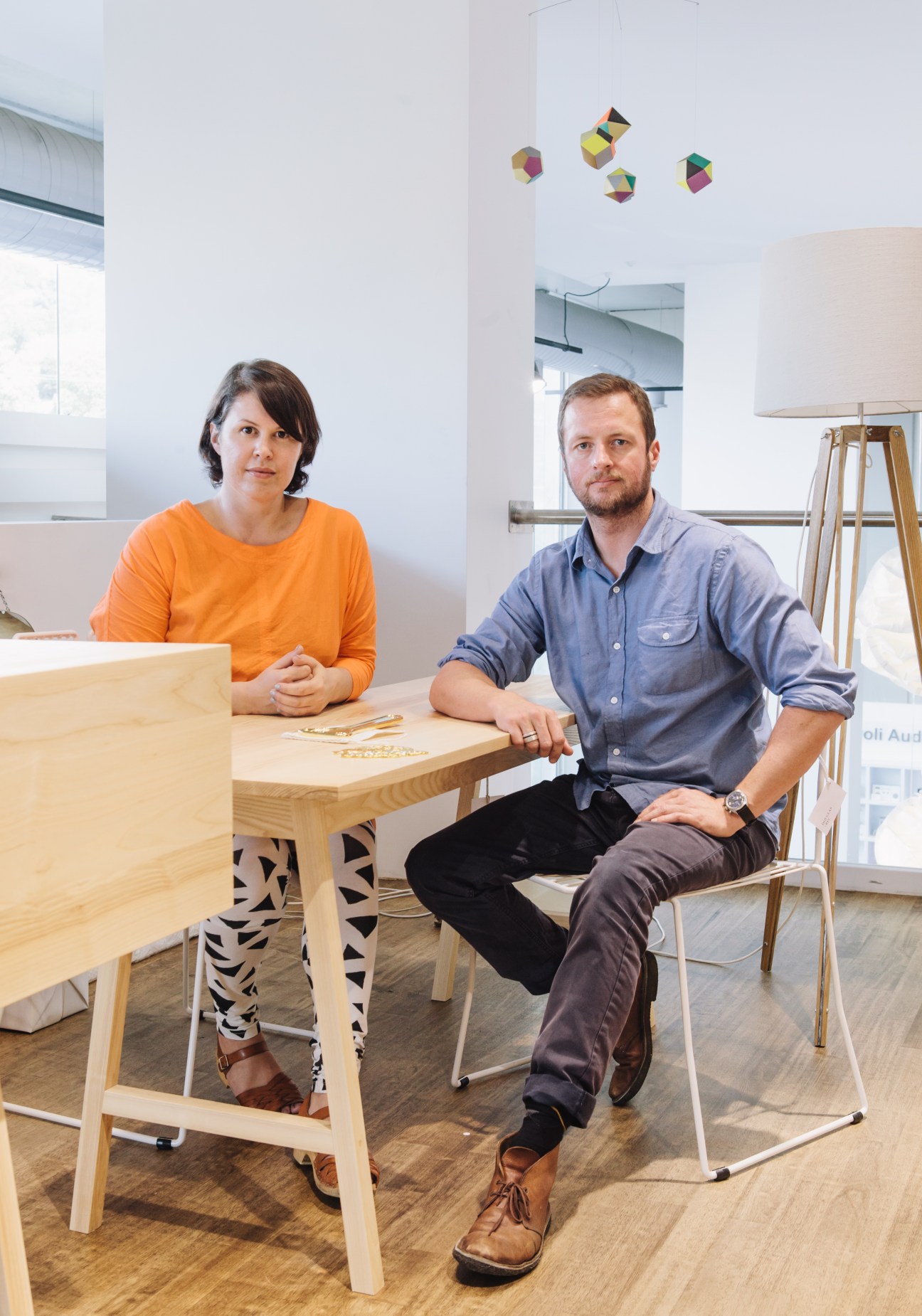 Rebecca Snelling and Paul Dowie sit at a wooden table in their design studio workshop.