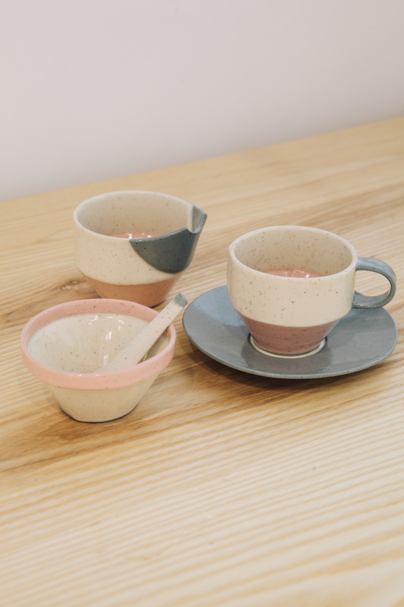 Handmade ceramic vessels with speckled glazes in cream and pink tones on a wooden surface.