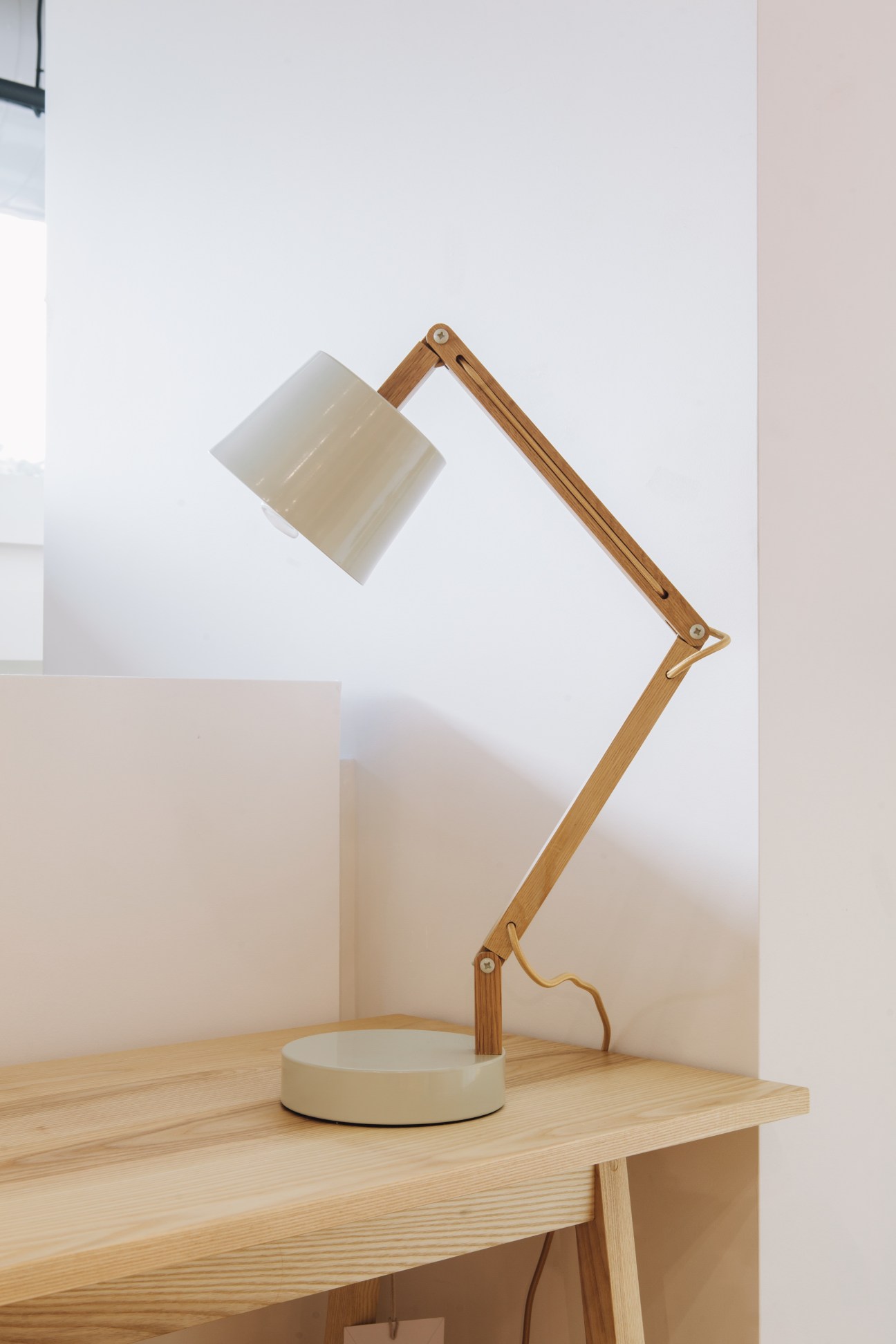 Wooden articulated desk lamp with frosted glass shade on a light wood surface.
