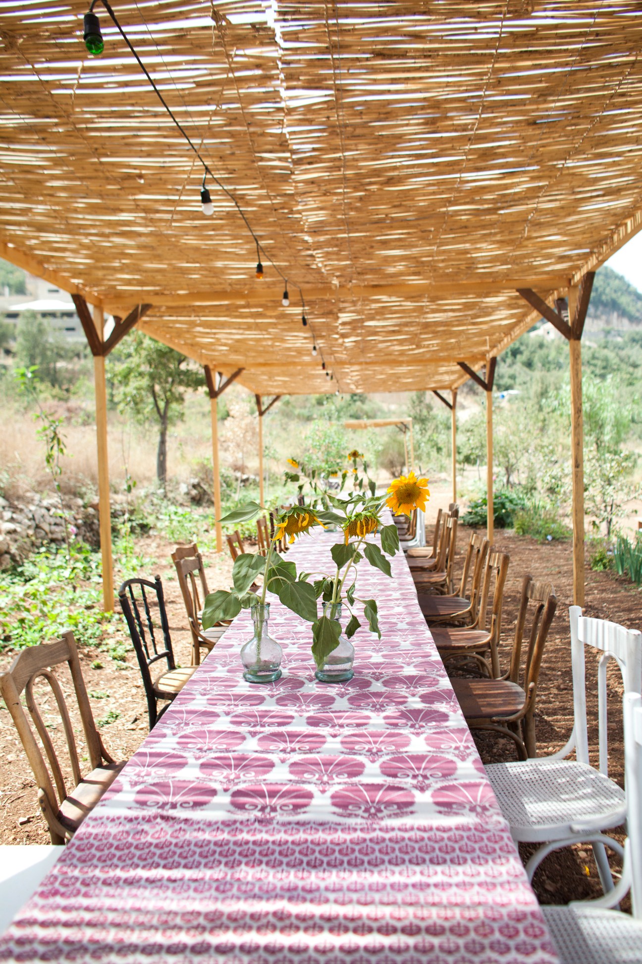 Outdoor dining table under wooden pergola with pink patterned runner and sunflowers in the Batroun Mountains.
