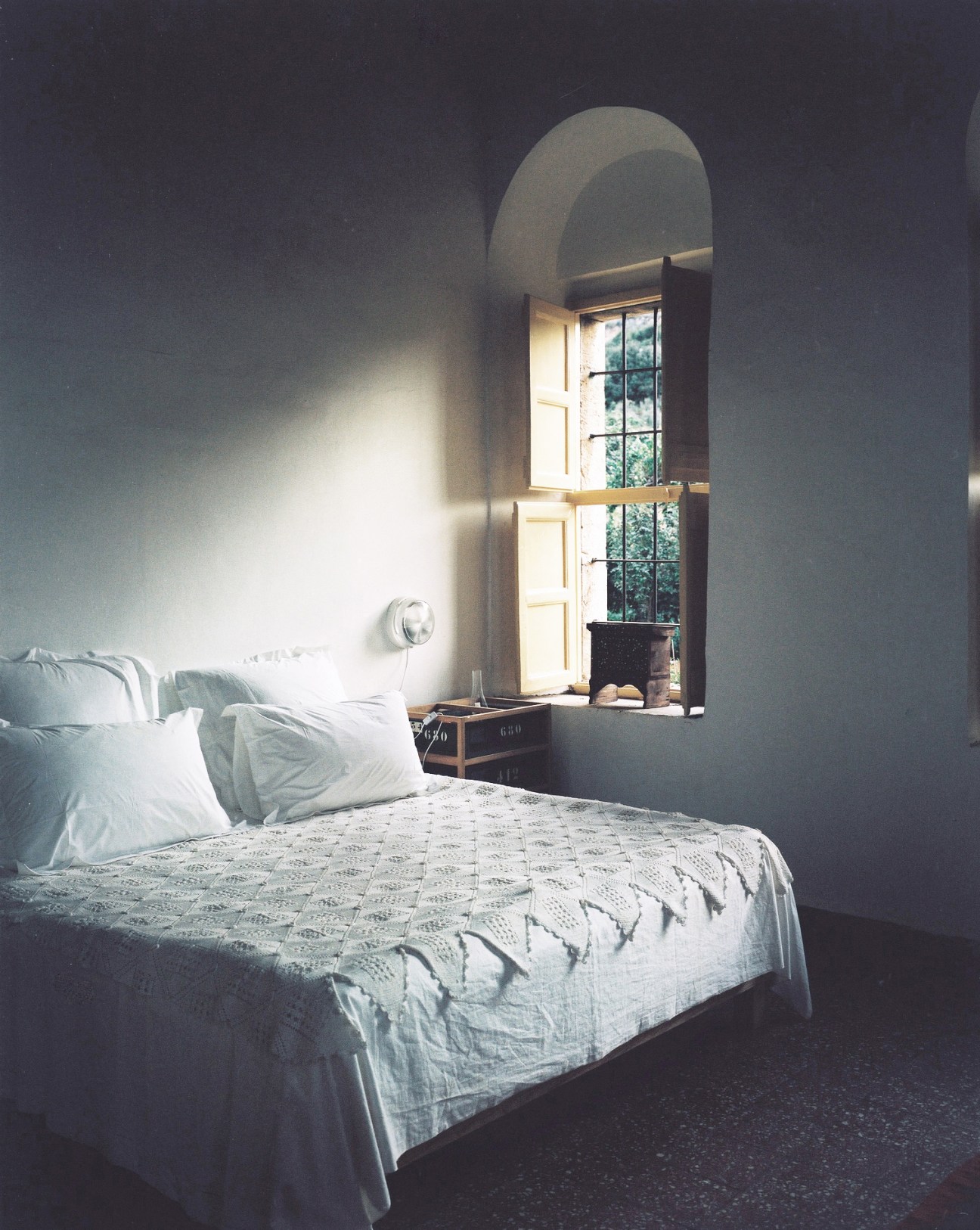 Sunlit bedroom with white bedding, arched window, and crocheted spread at Beit Douma