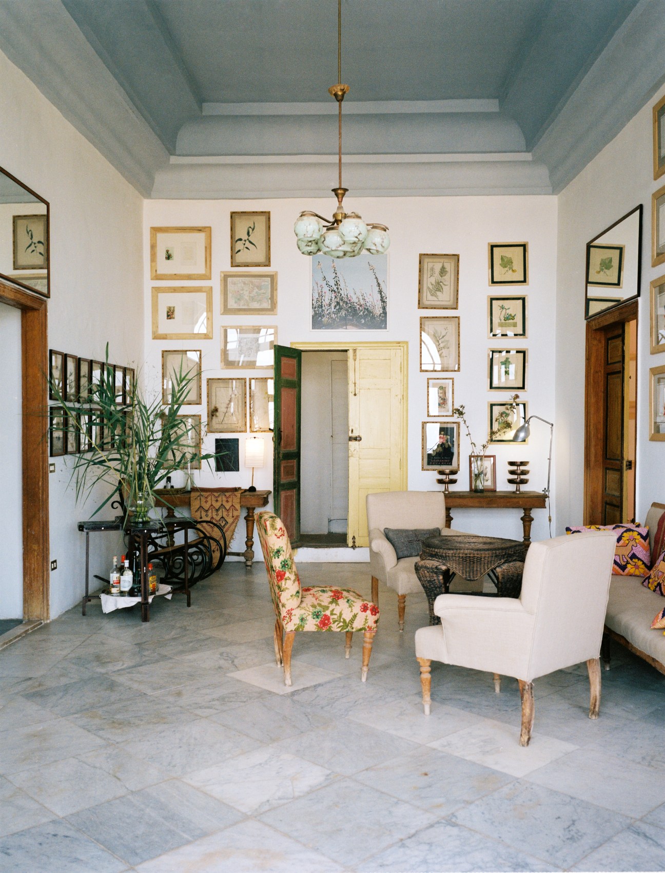 Airy hallway with pale blue ceiling, framed botanical prints, wooden doors, and vintage furnishings at Beit Douma.