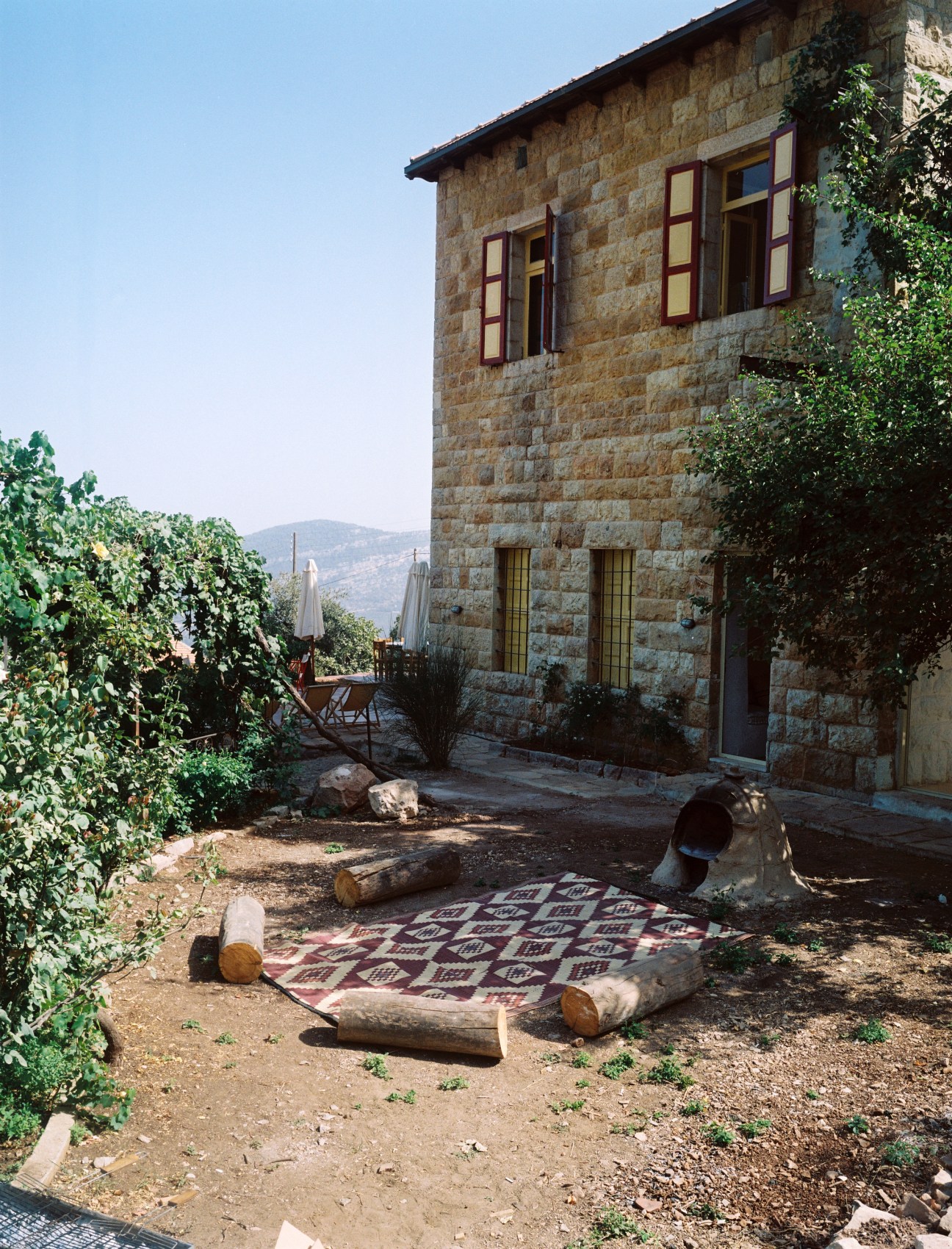 Traditional outdoor clay oven beside a stone house with red and yellow shutters in the Batroun Mountains.