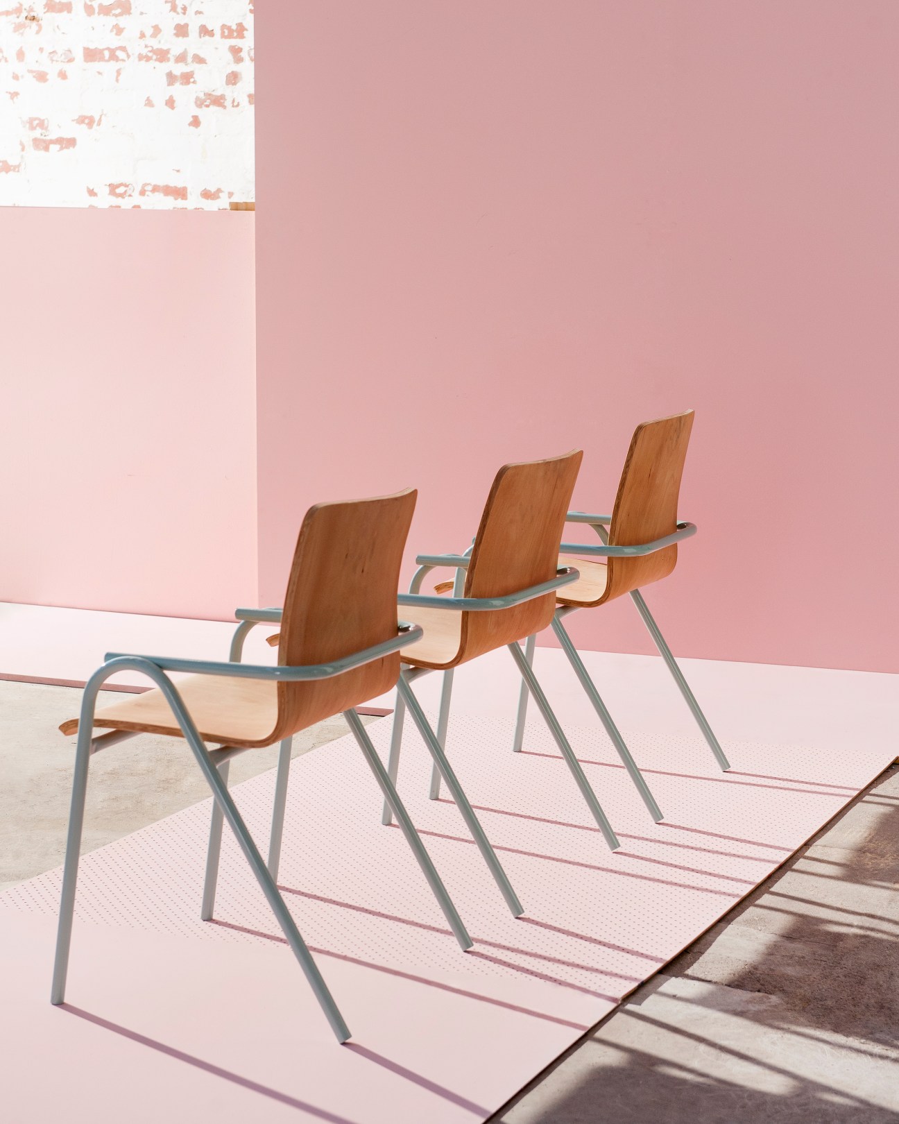 Three wooden chairs with metal frames arranged in a row against a pink wall.