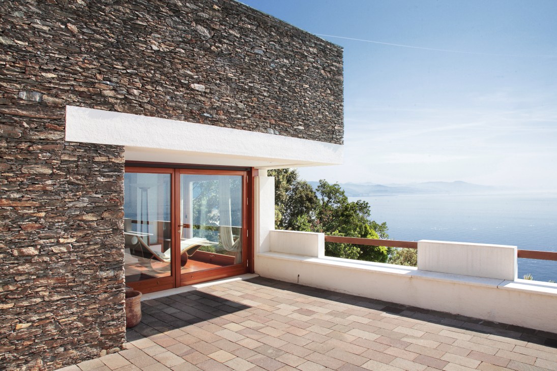 Modernist seaside villa with stone facade, white overhang, and terrace overlooking Mediterranean