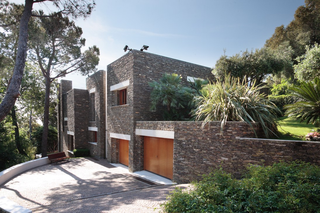 Modern stone villa with clean lines and angular design nestled among Mediterranean vegetation and trees.