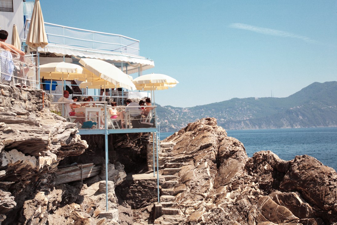 Bagni Sillo bathing spot with whitewashed cabanas, umbrellas and rocky coastline on Italian Riviera.