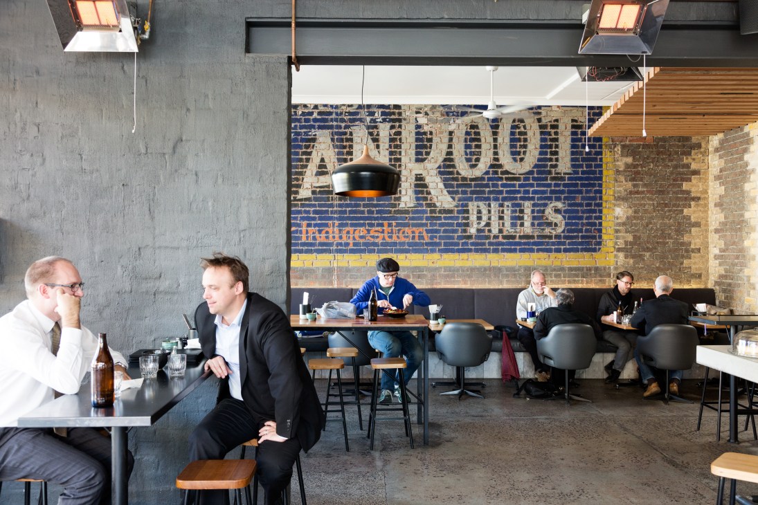 Interior of Dr Morse restaurant with exposed brick wall, industrial pendant lighting, and diners at wooden tables.