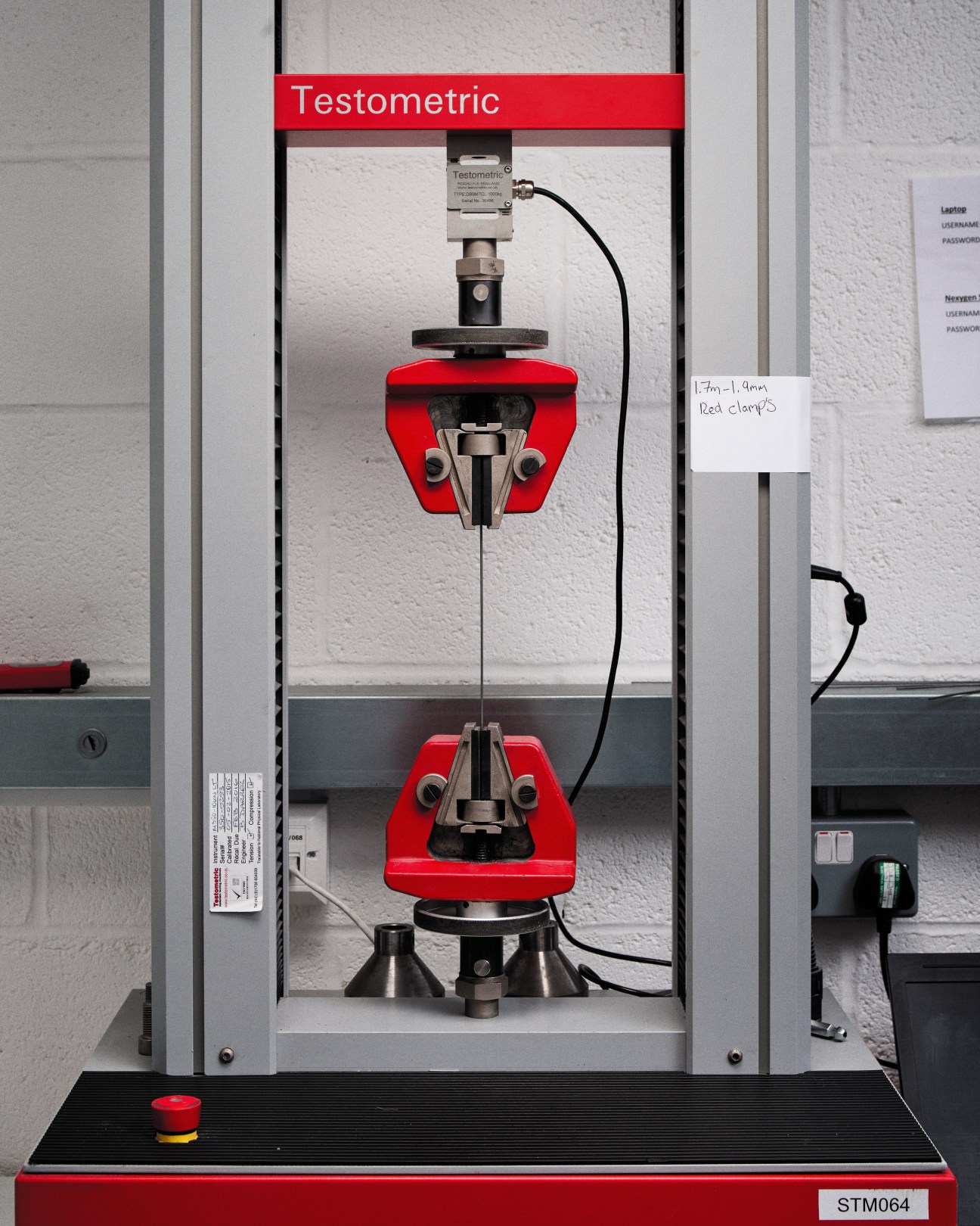 Testometric machine with red clamps testing the tensile strength of mattress spring wire.