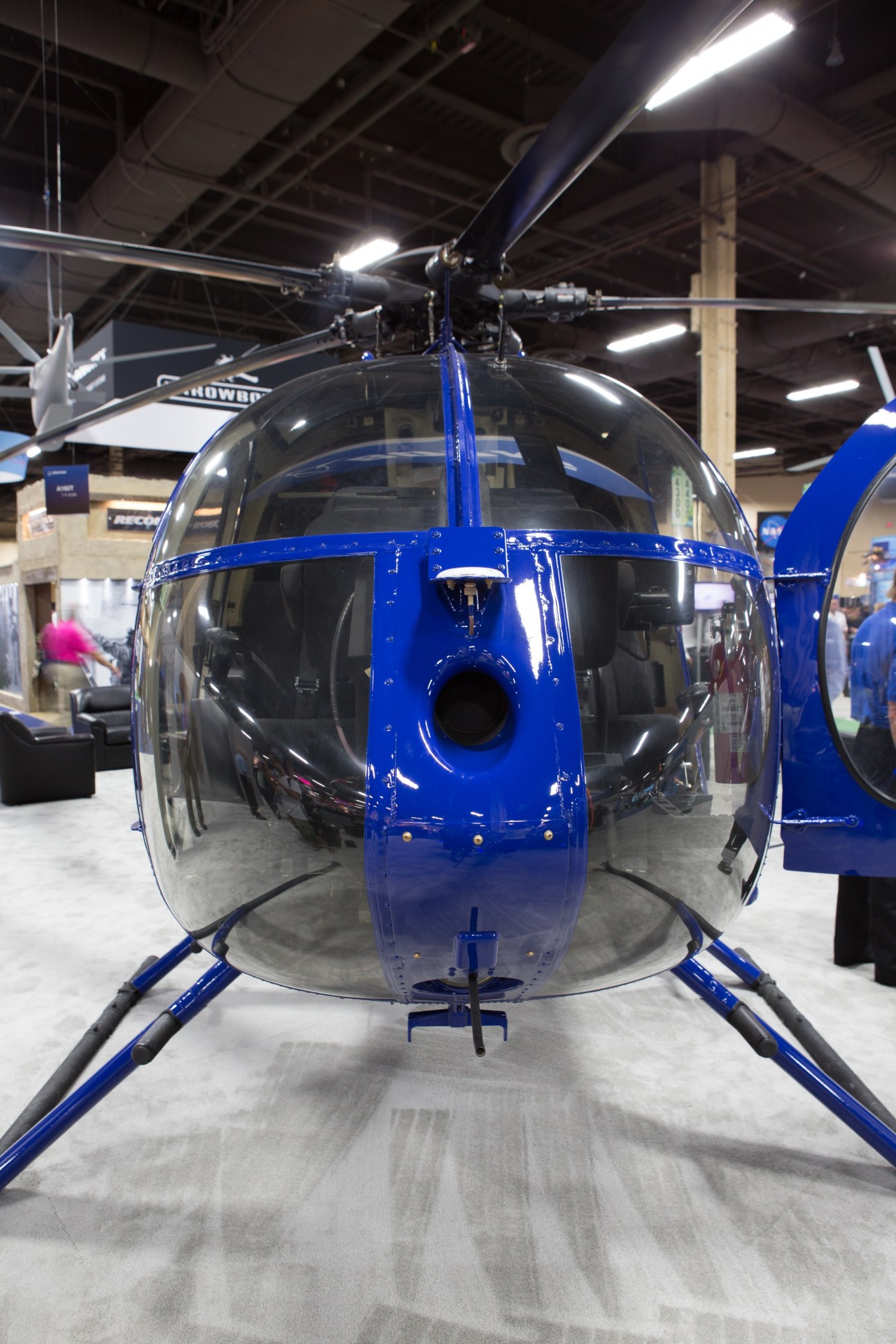 Blue Boeing unmanned helicopter drone displayed at trade fair with transparent cockpit and rotor blades visible from front view.