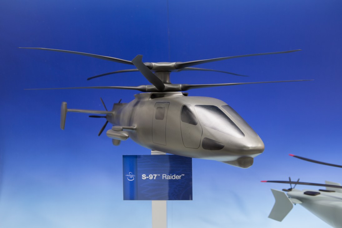 Sikorsky S-97 Raider unmanned helicopter model displayed against blue background.