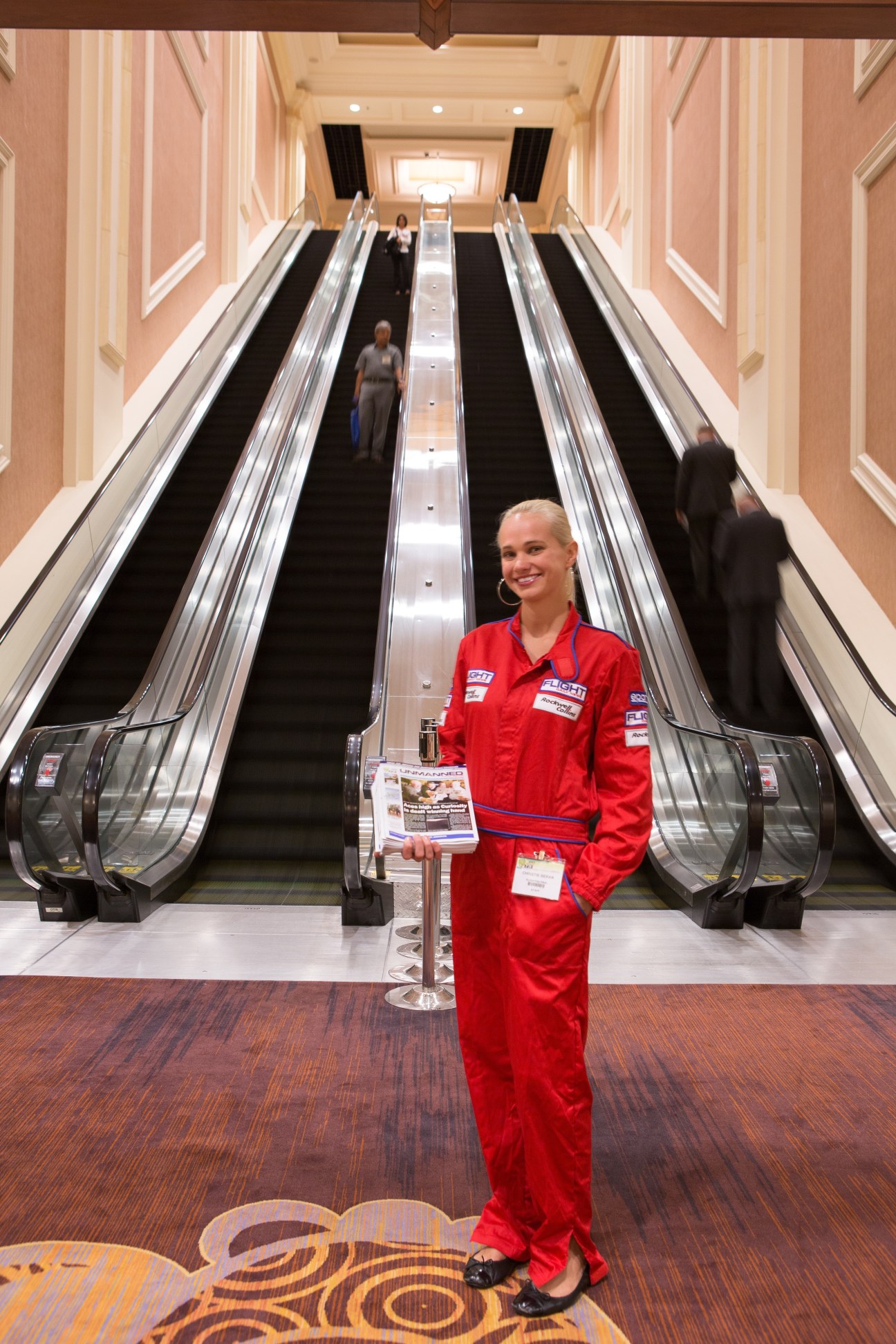 Woman in red jumpsuit standing in front of escalators at Unmanned Systems trade fair.