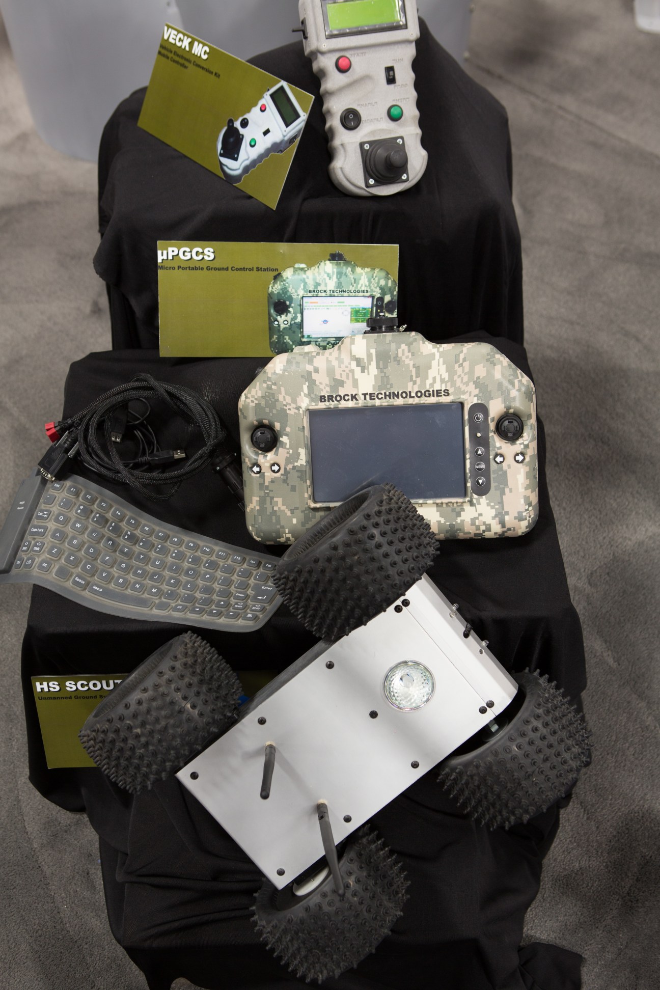 Overhead view of drone control systems and equipment displayed on black fabric, including Brock Technologies controllers and accessories.