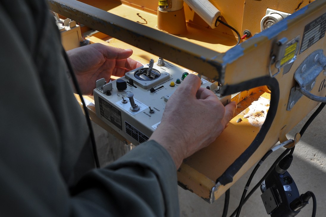 Operator's hands on a portable control panel with joystick and switches for flying a Heron 1 UAV.