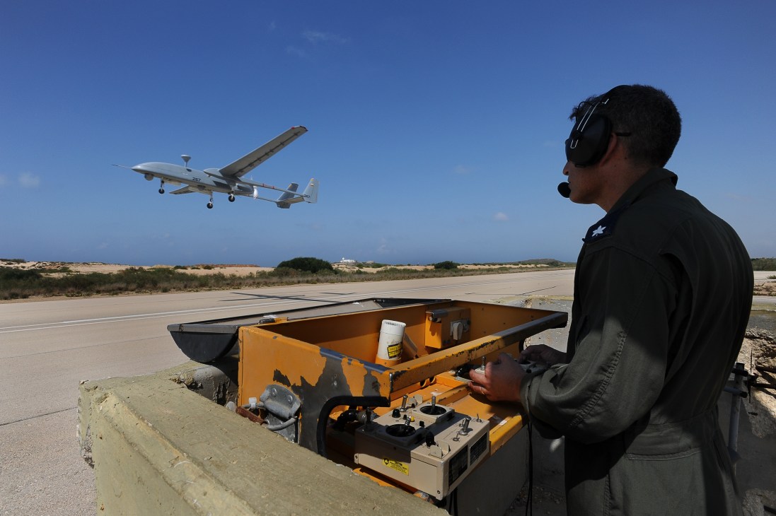 Israeli Air Force officer operates a Heron 1 UAV from portable ground control station as drone takes off from runway.