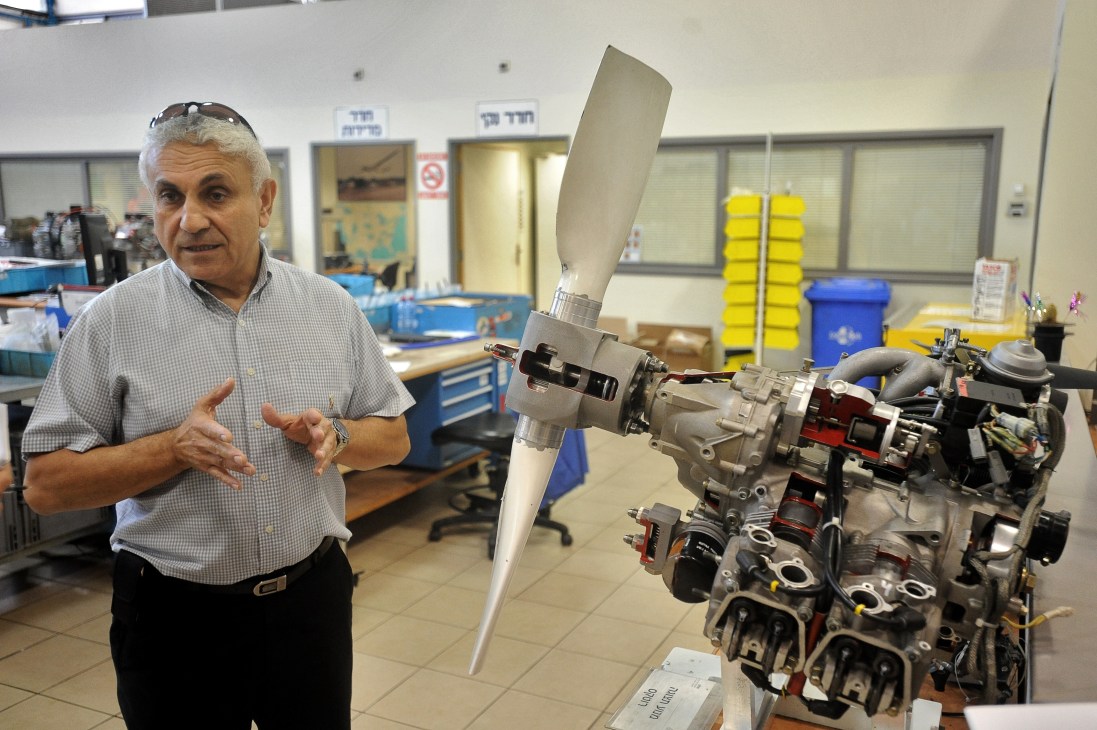 Tommy Silberring from Israel Aerospace Industries gestures while explaining UAV technology next to a drone engine component in a workshop.