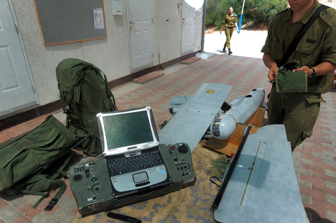 Israeli military personnel demonstrate a portable UAV control panel with laptop and joystick controller next to a small unmanned aerial vehicle.