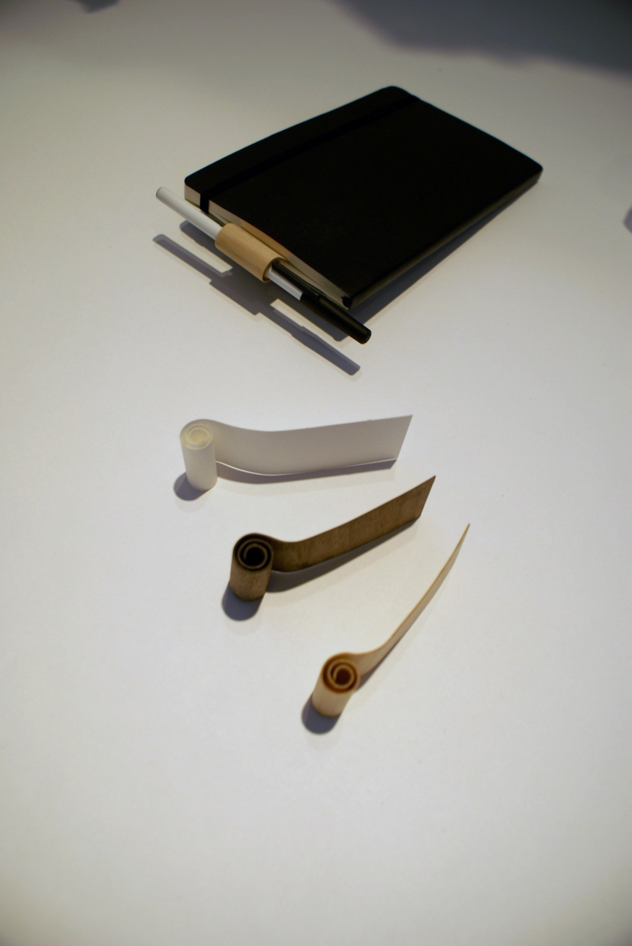 3-I design's Coppa penholder in various materials including paper and wood spirals with a black notebook above.