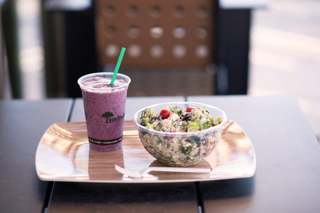 A purple smoothie drink with green straw and a fresh salad bowl on a wooden plate at Start Restaurant, Dallas.