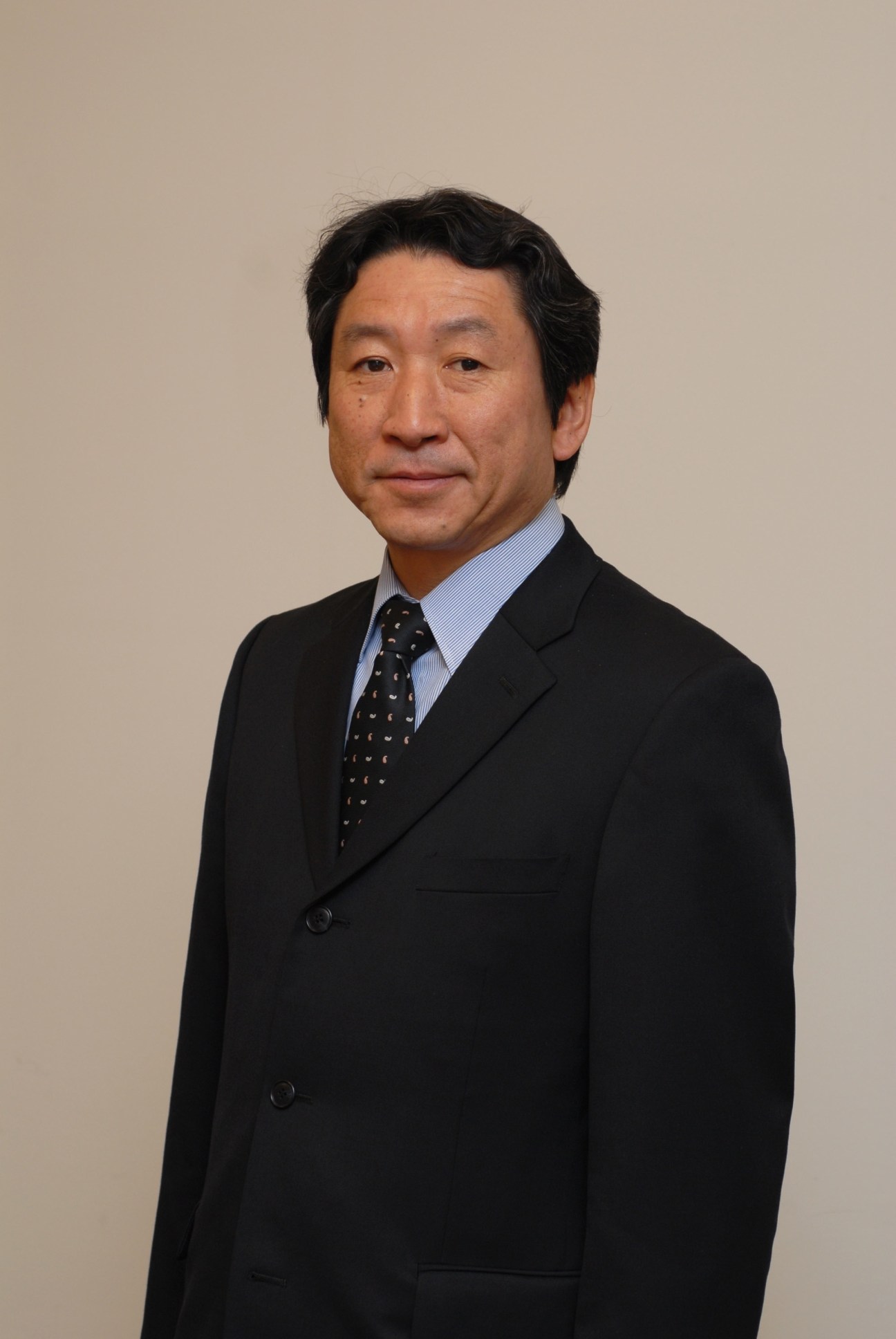 Portrait of Naoto Aiba, general manager for Mitsubishi's commercial development department, wearing a black blazer and blue shirt.