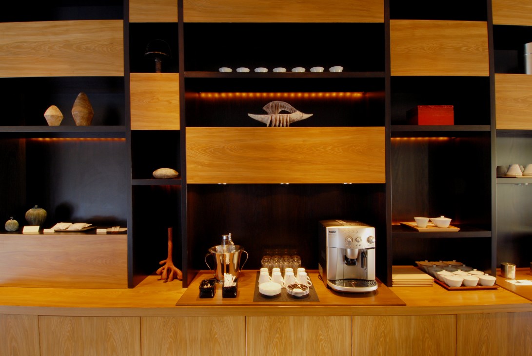 Modern hotel reception area with warm wood shelving, ambient lighting, and minimalist decorative objects displayed against black walls.