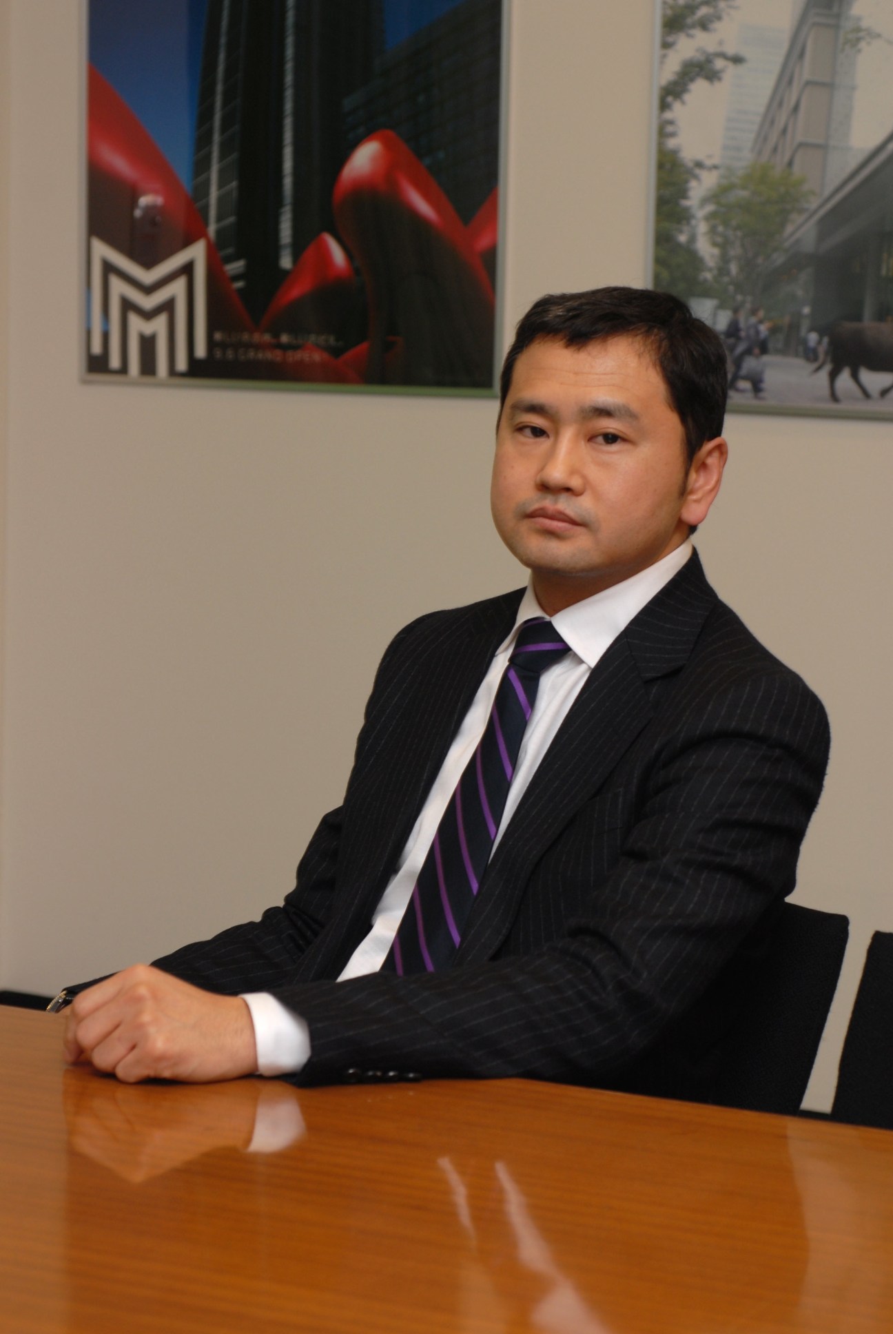 Tadamitsu Nakano, Mitsubishi commercial development manager, seated at a table wearing a dark pinstriped suit and purple tie.